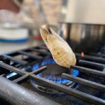 Phulka roti held with tongs over a gas flame